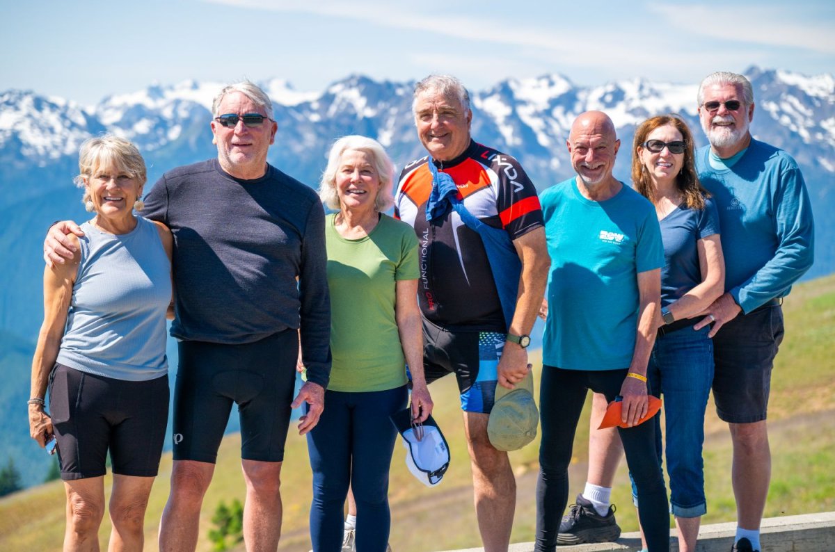 Group of people standing together in front of a snowy mountain range in biking clothes